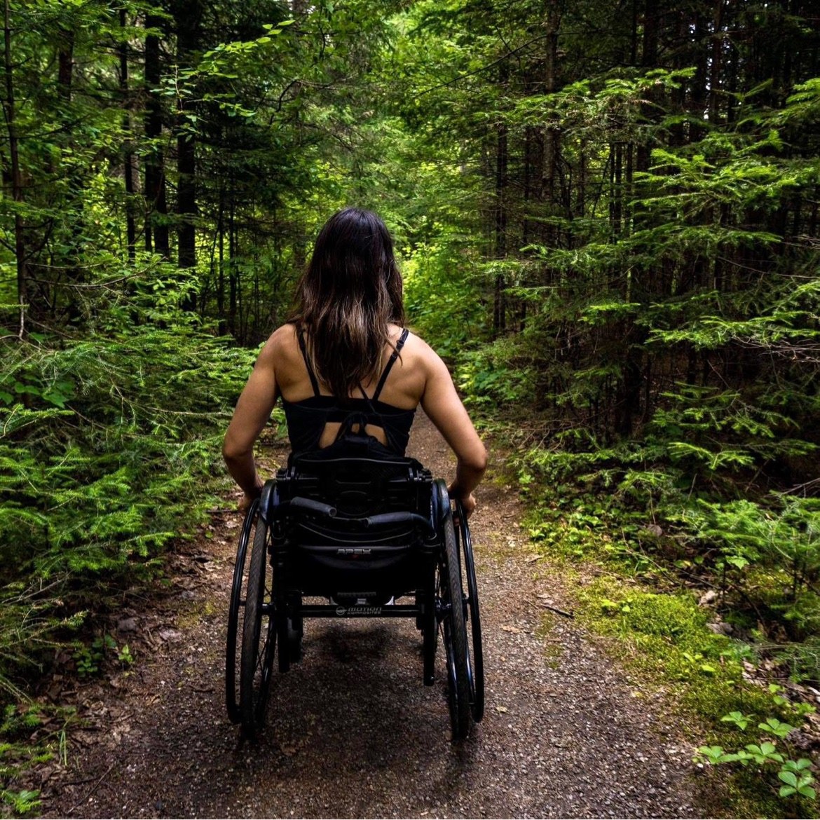Ollie Tremblay de dos en fauteuil roulant sur un sentier en forêt